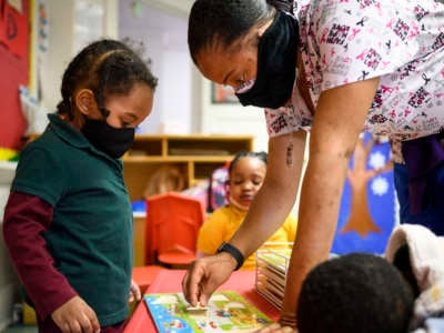 Shanikia Johnson, a teacher, helps a three-year-old clean up a puzzle at Little Flowers Early Childhood and Development Center in the Sandtown-Winchester neighborhood of Baltimore, Maryland, on January 12, 2021.