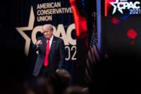 Donald Trump points at his fans in front of a large banner reading "CPAC"