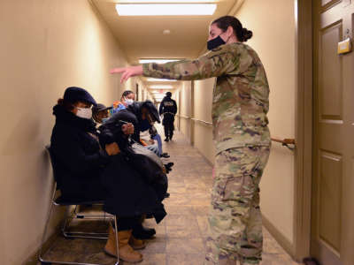 Someone in army camouflage directs seated patients