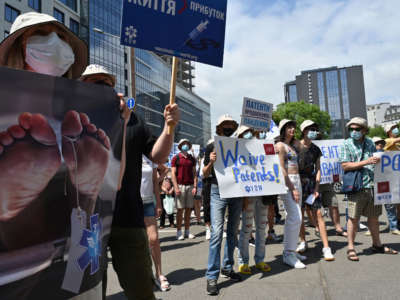 Activists hold placards reading "Patents kill", "Free vaccine" and "Waive patents" during a rally in Kiev, Ukraine, on July 2, 2021.