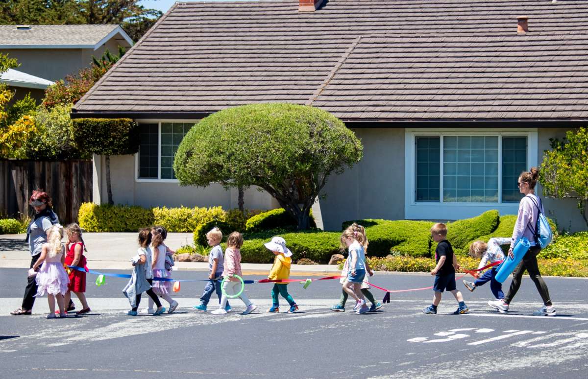 Children walk in a line to cross the street with adult supervision