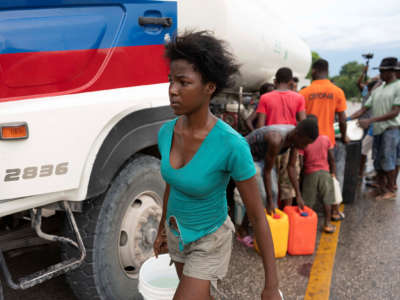 A young woman carries water away from a truck supplying it to a line of waiting people