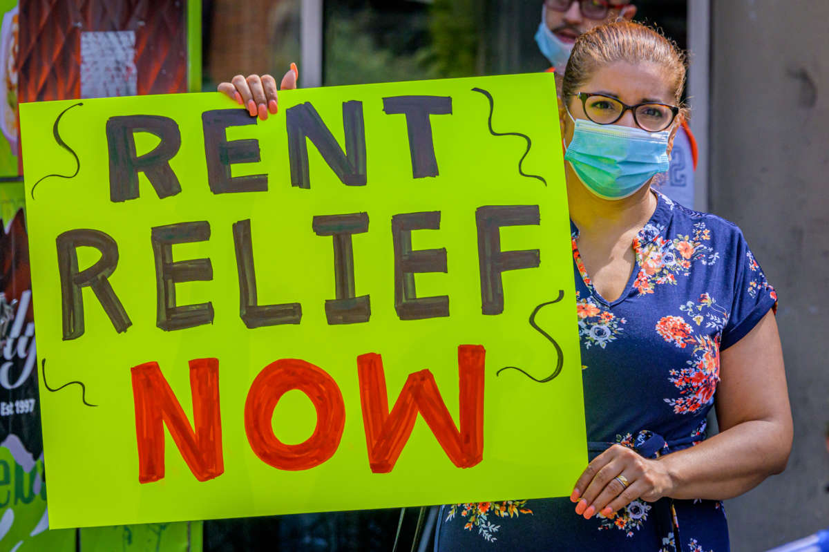 A woman holds a sign reading "RENT RELIEF NOW" during an outdoor protest