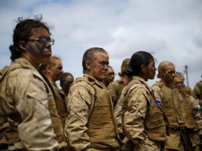 Mud-smeared female soldiers stand in a clump