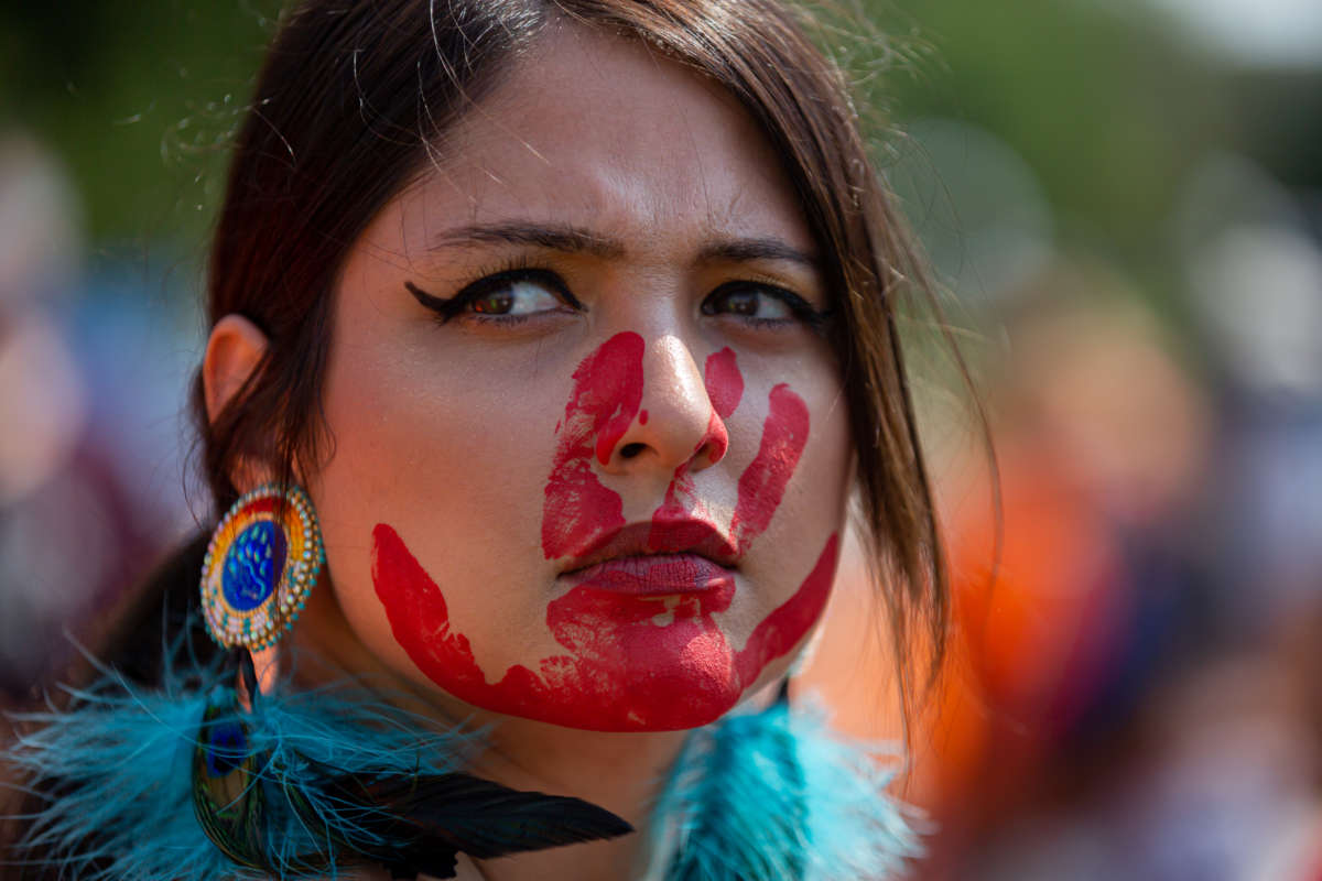 An Indigenous activist is seen with a painted red handprint over her mouth