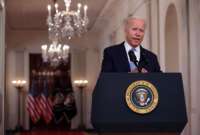 Joe Biden stands in front of glittering chandeliers