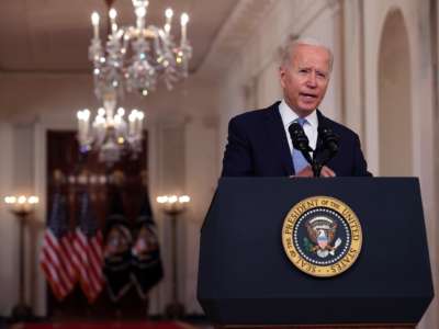 Joe Biden stands in front of glittering chandeliers