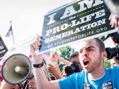 A man holds a pro-life sign and screams