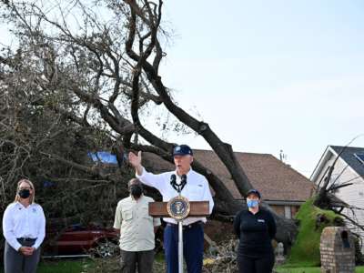 Joe Biden speaks in front of a home with a downed tree laying across its roof