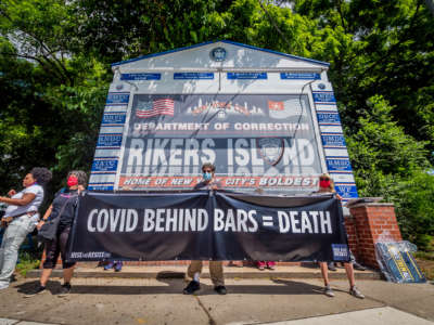 People display a sign reading "COVID BEHIND BARS = DEATH" during an outdoor protest