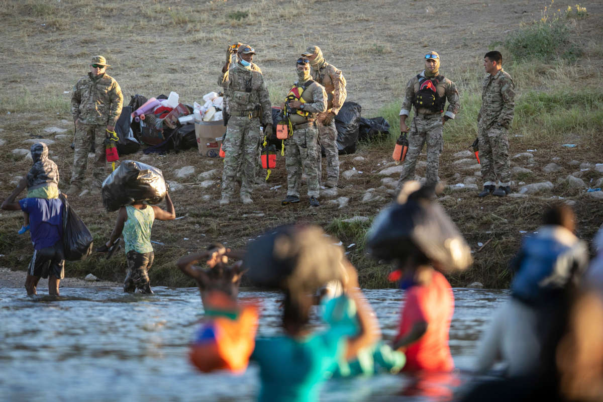 People carry their children and belongs across the rio grande while us custom and border patrol agents wait on the shore to harass them upon arrival