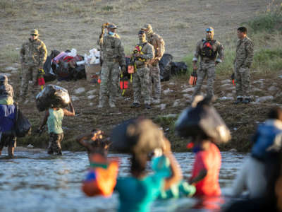 People carry their children and belongs across the rio grande while us custom and border patrol agents wait on the shore to harass them upon arrival