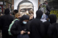 A mural of George Floyd peers over the heads of people walking on the sidewalk