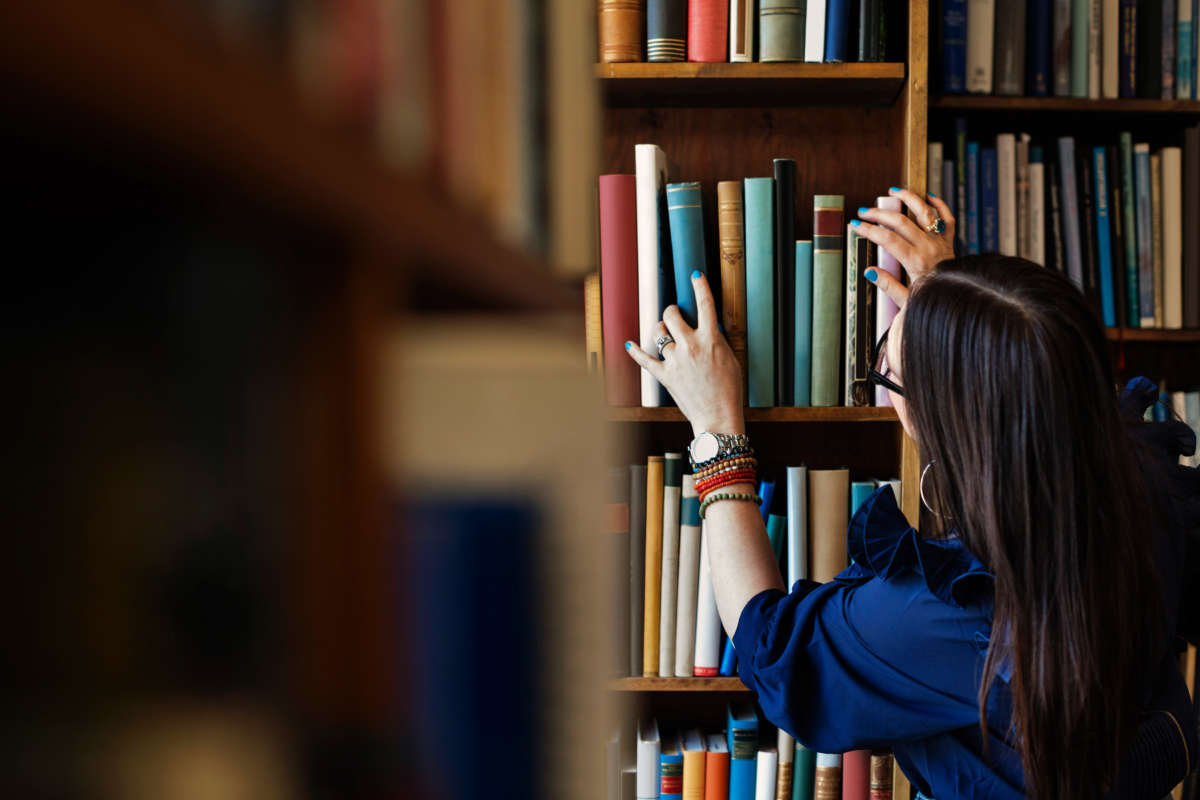 Woman reaches for book on shelves in library