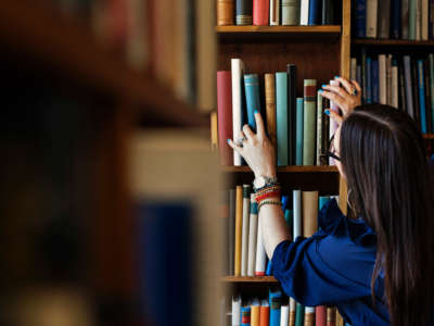 Woman reaches for book on shelves in library