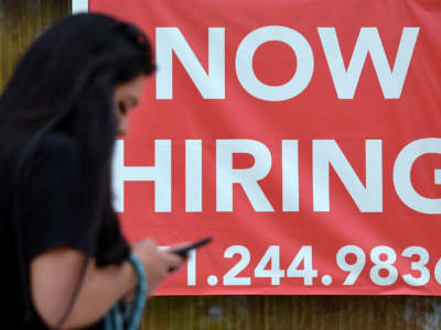 A woman walks by a "Now Hiring" sign outside a store on August 16, 2021, in Arlington, Virginia.