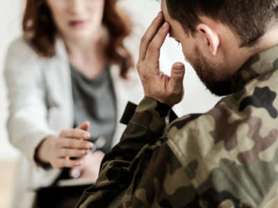 Soldier in military fatigues touches head as mental health professional reaches out