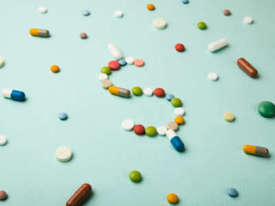 Pills, pharmacueticals arranged in shape of dollar sign on pale green background