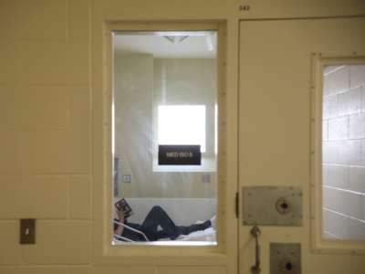 A prisoner is seen reading a book through the narrow window of their cell door