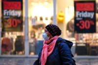 A woman in a mask and cold weather clothes walks past mall sineage