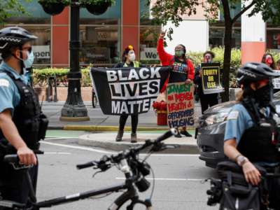 A woman holds a Black Lives Matter flag along with protesters holding signs during the Occupy City Hall Protest and Car Caravan hosted by Chicago Teachers Union in Chicago, Illinois, on August 3, 2020.