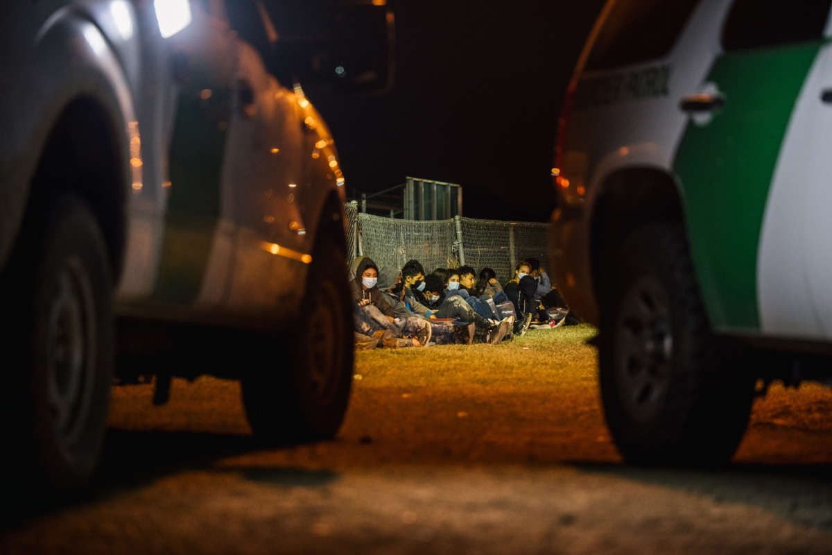 Migrants sit against a fence while waiting to board a border patrol bus after crossing the Rio Grande into the U.S. on November 17, 2021, in La Joya, Texas.