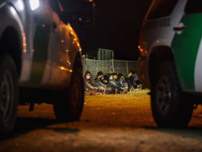 Migrants sit against a fence while waiting to board a border patrol bus after crossing the Rio Grande into the U.S. on November 17, 2021, in La Joya, Texas.