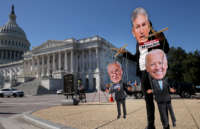 A demonstrator wearing a Joe Manchin mask plays puppet-master to Chuck Schumer and Joe Biden puppets outside the U.S. Capitol