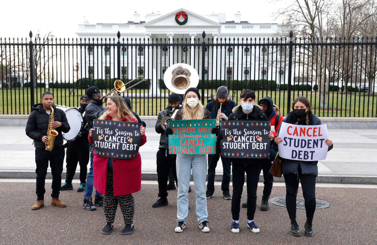 Activists hold festive signs calling on President Biden to cancel student debt and not resume student loan debt while musicians play joyful music, greeting the White House staff as they arrive to work on December 15, 2021, in Washington, D.C.