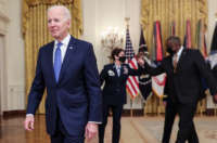 President Joe Biden walks out of the podium after speaking during International Women's Day in the East Room of the White House in Washington, D.C., on March 8, 2021. Behind Biden, Defense Secretary Lloyd Austin and Air Force General Jacqueline Van Ovost greet each other with an elbow-bump.