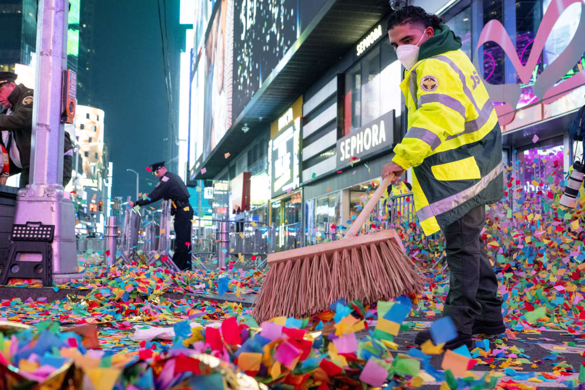 A masked worker sweeps up confetti from a new year celebration