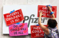 A woman tapes protest signs to the Pfizer sign during a protest at the Pfizer Pharmaceuticals Headquarters on July 14, 2021, in Manhattan in New York City.