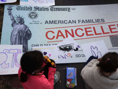 Children draw on top of a cancelled check prop during a rally in front of the U.S. Capitol on December 13, 2021, in Washington, D.C.