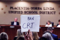 A person holds a sign reading "BAN CRT" during a school board meeting