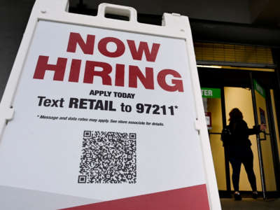 A woman walks past a "Now Hiring" sign in front of a store on January 13, 2022, in Arlington, Virginia.
