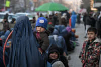 A woman wearing a burqa carries an infant as she waits with others for free bread in front of a bakery in Kabul, Afghanistan, on January 24, 2022.