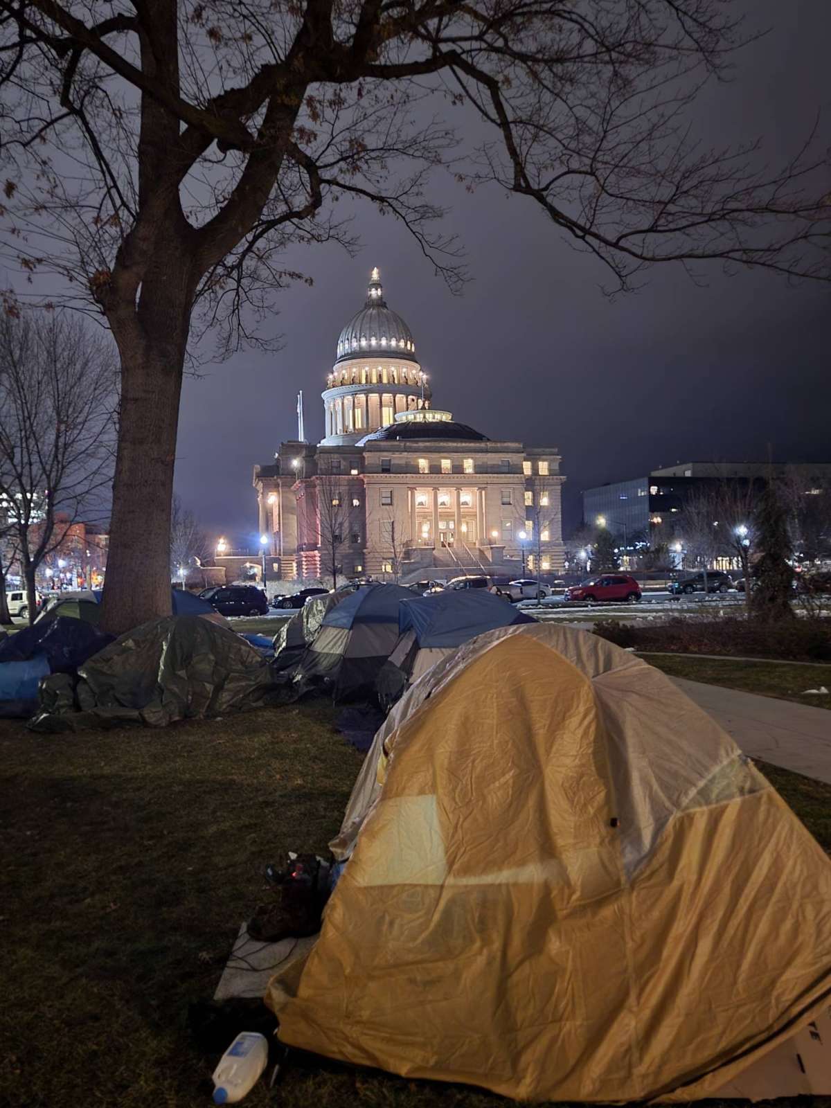 The lights of the state capitol in Boise, Idaho, can be seen beyond tents pitched by Boise Mutual Aid activists and the unhoused community.