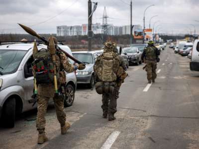 Ukrainian servicemen carry rocket-propelled grenades and sniper rifles as they walk towards the city of Irpin, Ukraine, on March 13, 2022.