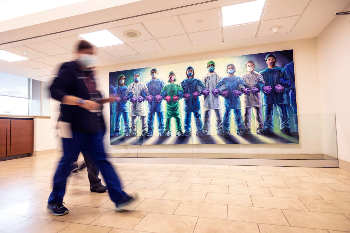 People hurriedly walk past a mural depicting health care workers linking arms