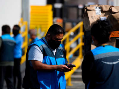 An Amazon delivery driver scans bags of groceries while loading a vehicle outside of a distribution facility on February 2, 2021, in Redondo Beach, California.