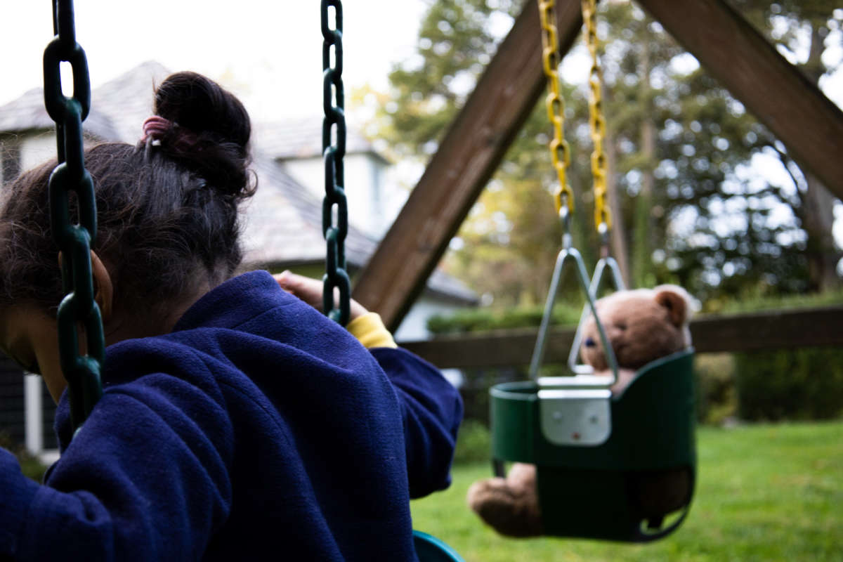 Child on swing set with teddy bear