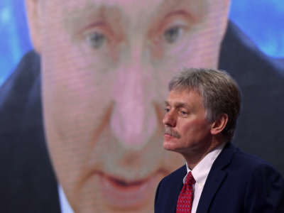 Kremlin spokesman Dmitry Peskov sits in front of a screen displaying Russian President Vladimir Putin addressing his annual press conference via a video link from the Novo-Ogaryovo state residence, at the World Trade Center's congress center in Moscow on December 17, 2020.