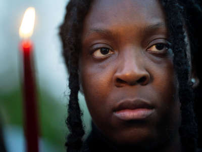 A close-up portrait of a Black woman holding a red candle