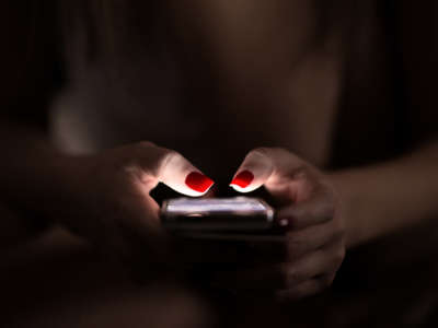 Person with red fingernail polish uses cell phone in the dark