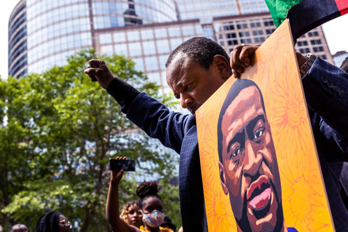 A man raises a fist while holding a portrait of the late George Floyd while at an outdoor protest