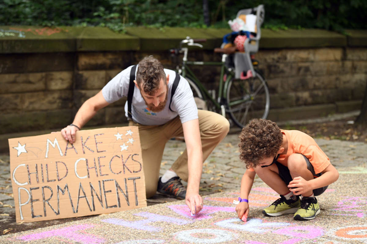 A father and child use chalk to write messages in support of the expanded child tax credit