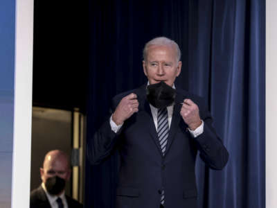 President Joe Biden removes his face mask in the South Court Auditorium of the White House on March 31, 2022, in Washington, D.C.