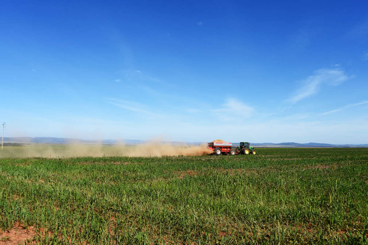 A tractor drives through a feild, spreading dust in its wake
