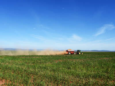 A tractor drives through a feild, spreading dust in its wake