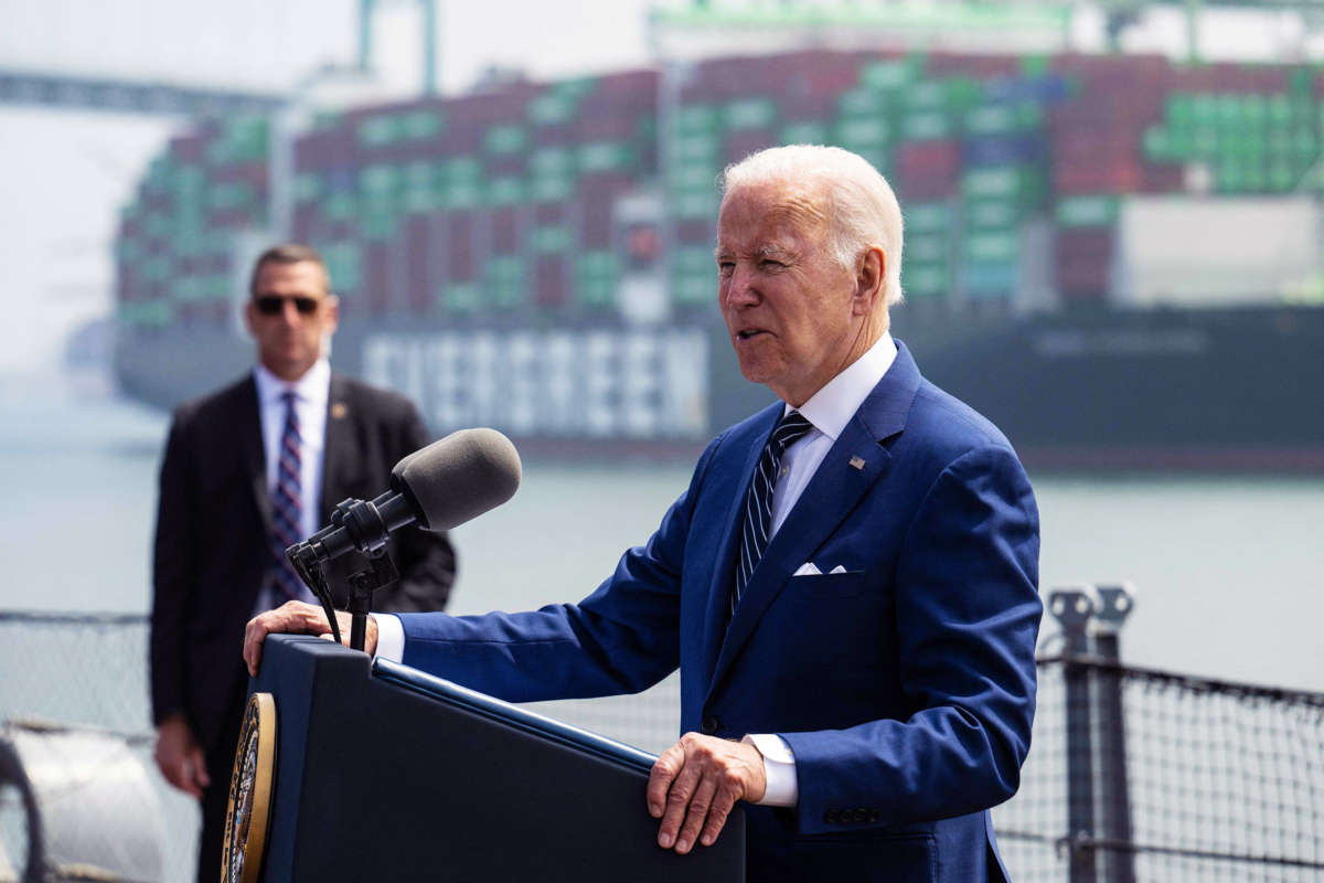 Joseph Robinette Biden speaks into a microphone at a podium near commercial docks